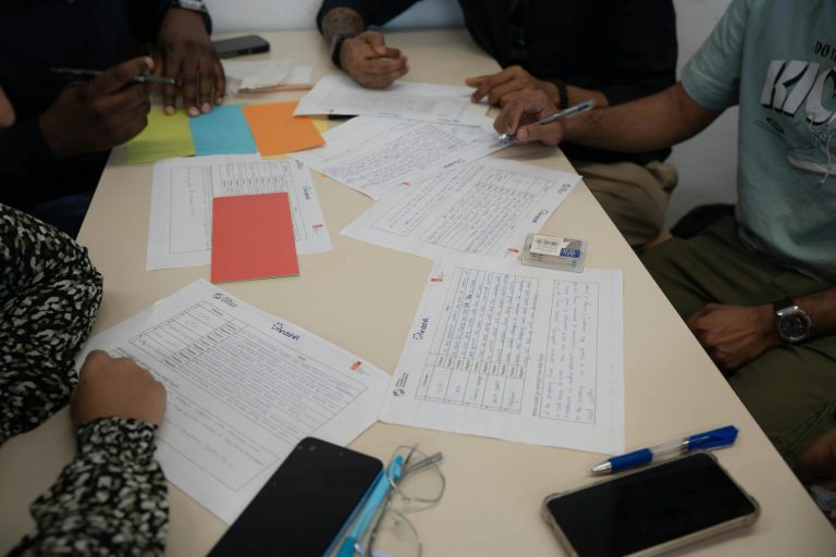 Professional meeting room scene with warning signs and red flags visible on documents spread across a conference table. Business people in suits examining paperwork with magnifying glasses, looking concerned and vigilant. Bright office lighting, modern corporate environment. Keywords: business meeting, warning signs, documents, professional — Formations 90
