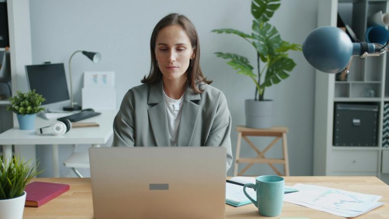 Professional woman in her 40s sitting at a modern workspace, looking thoughtfully at a laptop screen displaying career options and digital tools. Bright, organized office environment with plants and natural light. She has notebooks and a coffee cup nearby, suggesting career planning and decision-making. Warm, encouraging atmosphere that conveys professional growth and new opportunities. Keywords: career change, professional development, modern office, planning — Formations 90